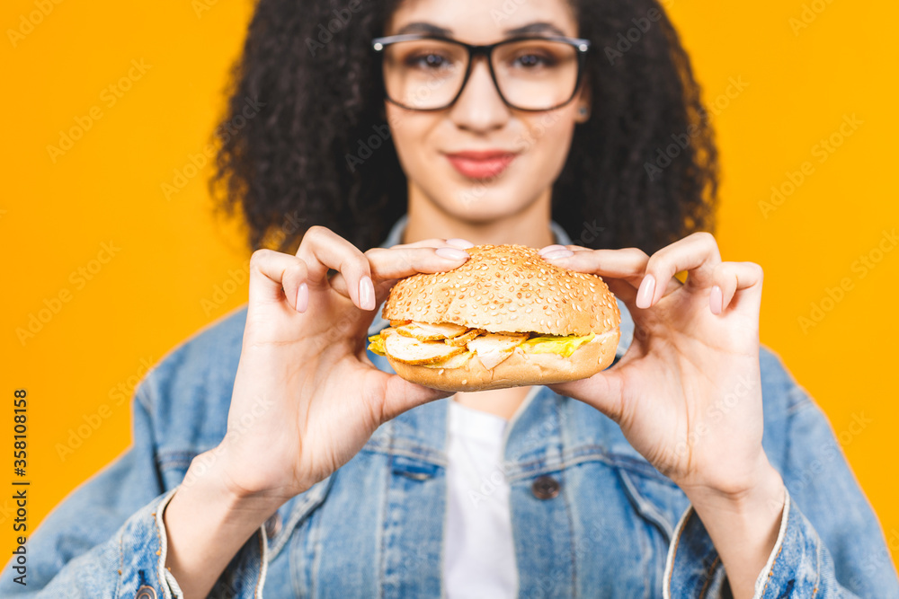 African American black young woman eating hamburger isolated on yellow background. African American black young woman eating hamburger isolated on yellow background.