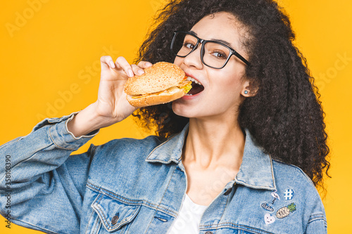 African American black young woman eating hamburger isolated on yellow background.