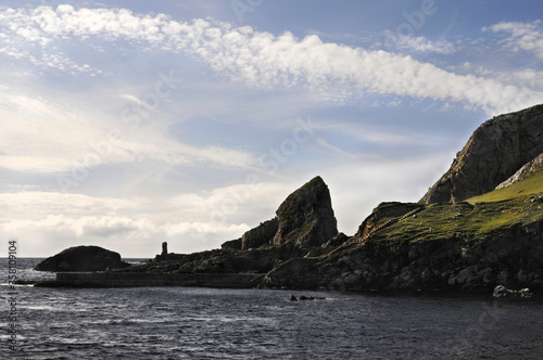 Magnifique crique sertie de rocher et de falaises noires donnant sur la mer au nord de l'Irlande. Le coucher du soleil et les nuages donnant un aspect sauvage et dramatique à ce paysage.
