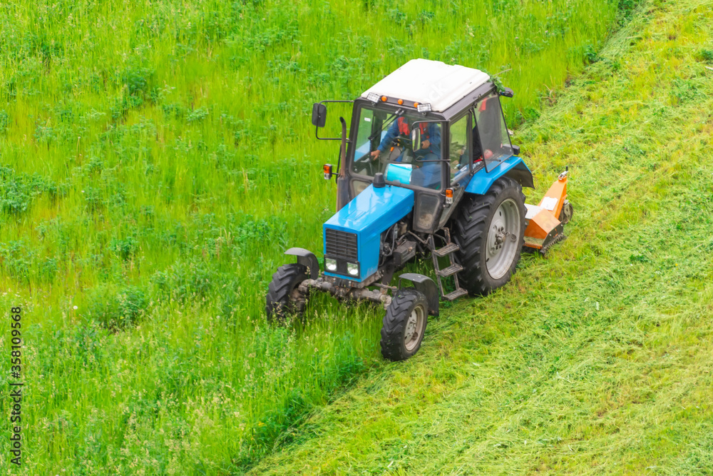 Tractor uses trailed lawn mower to mow grass on city lawns, aerial view. Tractor uses trailed lawn mower to mow grass on city lawns, aerial view.