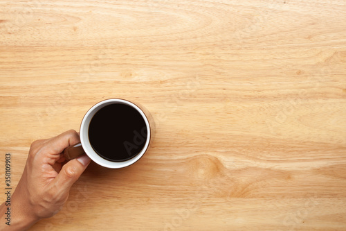 Hand holding a cup of coffee on wooden table. Top view and copy space