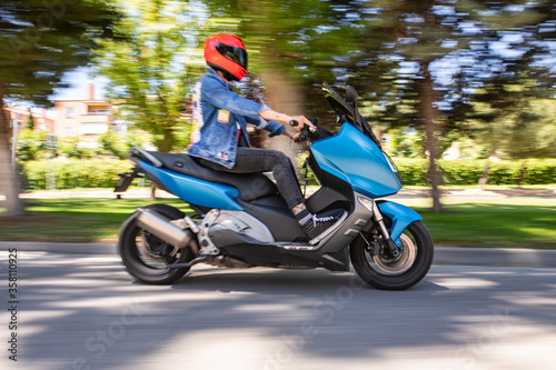 Moto tipo scooter circulando por una calle con arboles y día soleado photo