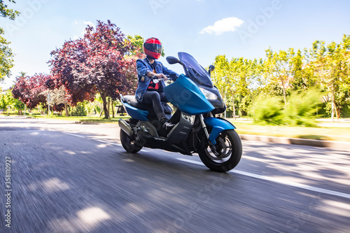 Moto tipo scooter circulando por una calle con arboles y día soleado photo