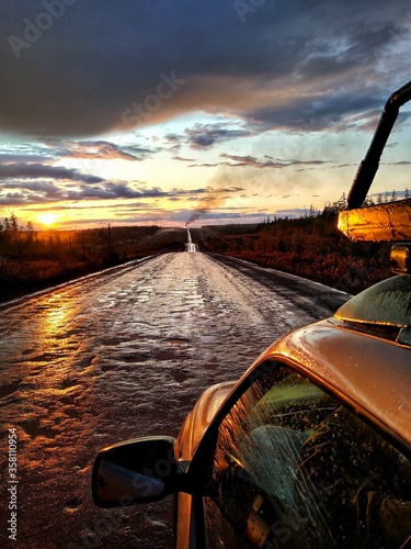 Traveling by car on a dirt country road to sunset after rain