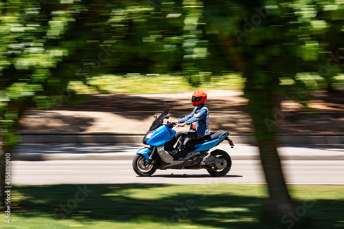 Moto tipo scooter circulando por una calle con arboles y día soleado photo