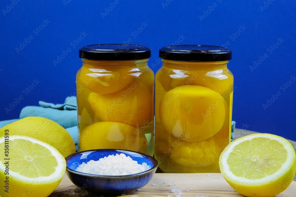 Preparation of moroccan preserved pickled salt lemons: Close up of isolated sliced yellow citrus fruits, blue bowl and wooden spoon with coarse sea salt grains on wood cutting board Preparation of moroccan preserved pickled salt lemons: Close up of isolated sliced yellow citrus fruits, blue bowl and wooden spoon with coarse sea salt grains on wood cutting board