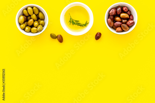 Olive oil in bowl near oilves on yellow desk from above copy space