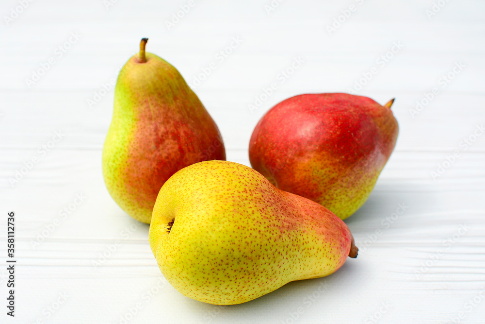 Three ripe juicy pears on a white wooden background. Close-up. Three ripe juicy pears on a white wooden background. Close-up.