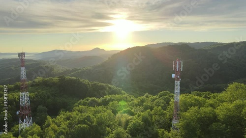Aerial view of 5G telecom tower antenna for data internet wireless smartphone generation, ubicated in the middle of a green forest during an epic sunrise in a mountain landscape photo