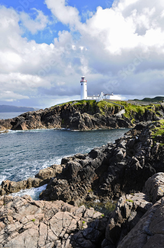 Magnifique phare blanc posé sur des falaises rocheuses et verdoyantes au bord de la mer bleu indigo de l'Irlande du nord.