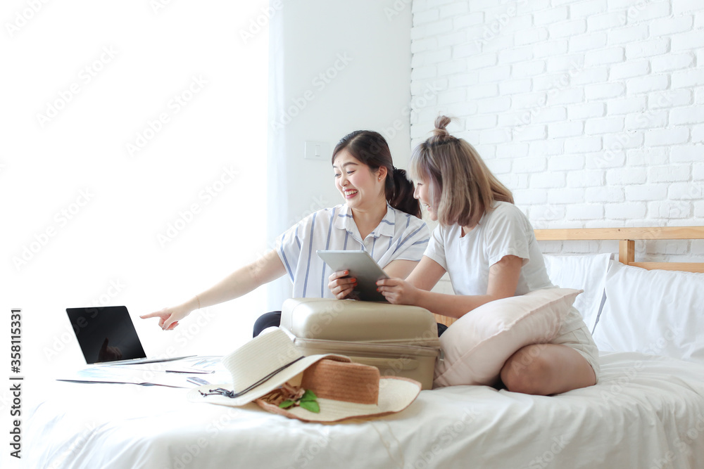 Tourism concepts. Two young women are happy with the success of their booking. Two girl rejoicing while holding passport and travel tickets. Young female looking tablet and laptop computer.
