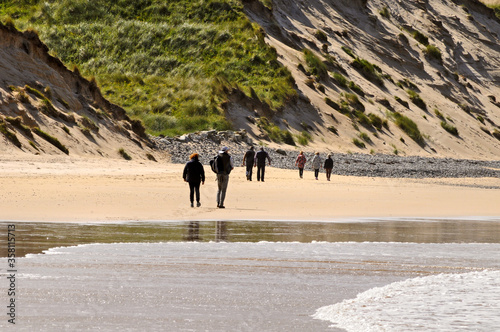 Promeneurs sur une plage de sable et sur fond de dunes couvertes de végétation au nord de l'Irlande.