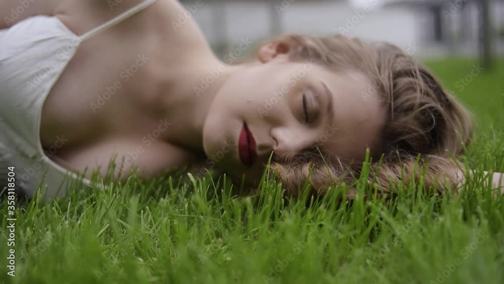 A teenager girl lies on the grass in a beautiful white dress, rests, enjoys nature. Girl with short blond hair. Beautiful and healthy skin Girl sleeping outdoors A teenager girl lies on the grass in a beautiful white dress, rests, enjoys nature. Girl with short blond hair. Beautiful and healthy skin Girl sleeping outdoors