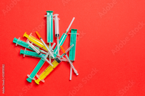 Top view of a heap of syringes and insulin syringes at red background. Medical injection concept with copy space