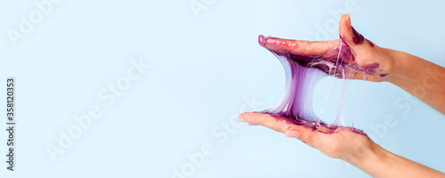 Young girl hands with sticky purple slime on blue background, liquid wax for depilation, conceptual flyer banner with copy space, antistress relax, modern kids hobby oddly satisfying semi surreal asmr
