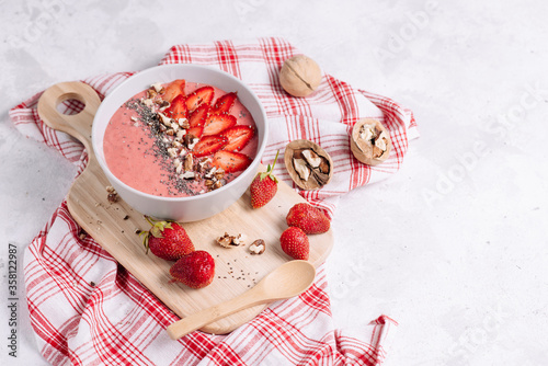 Strawberry smoothie in a plate with milk and ice cream and walnuts, soup on a wooden board with a beautiful serving of red napkin and berries on a light background. Still life with place for text.