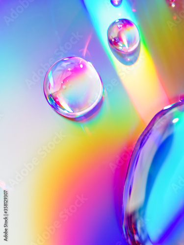 Abstract composition. Drops of liquid are on an iridescent surface. Slightly defocused image. Trending background of saturated colors and gradients.