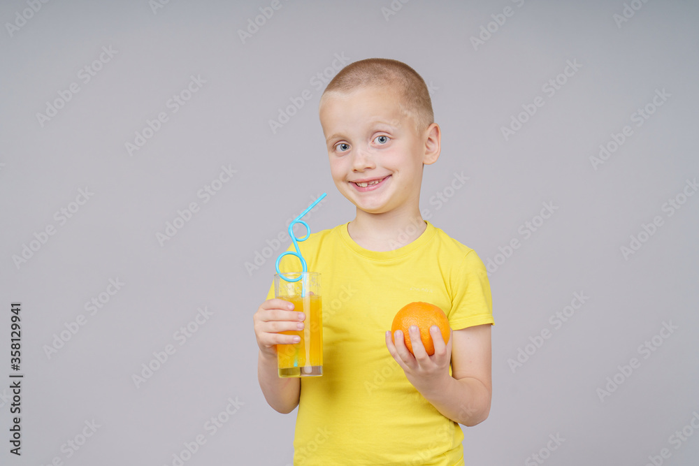 Smiling boy standing with fruit orange and drink. Isolated on gray Smiling boy standing with fruit orange and drink. Isolated on gray