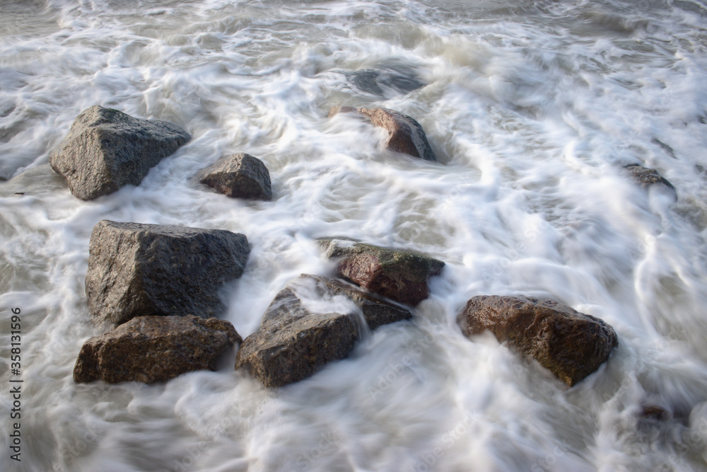 Long exposure seascape waves on the stones. A slow shutter speed was used to see the movement ( Soft focus shot)