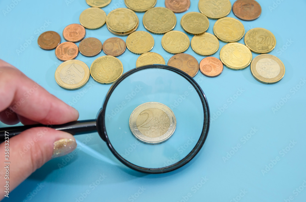 Fototapeta premium 2 euro coin through a magnifying glass. Blue background. Financial concept. Lots of coins. Savings concept.