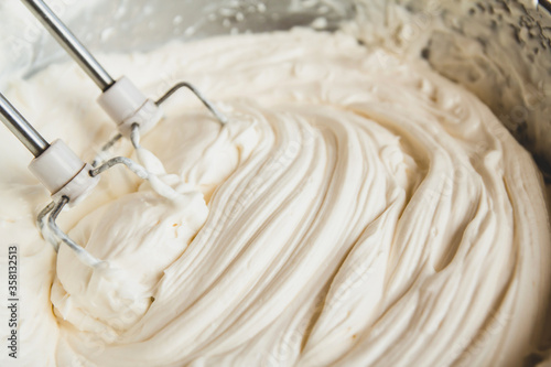 White butter cream in a metal bowl. Beating cream cake. Mixer whisk in cream.