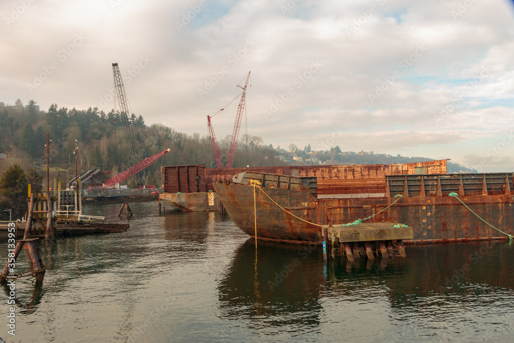 Rusting cargo barge with background cranes.