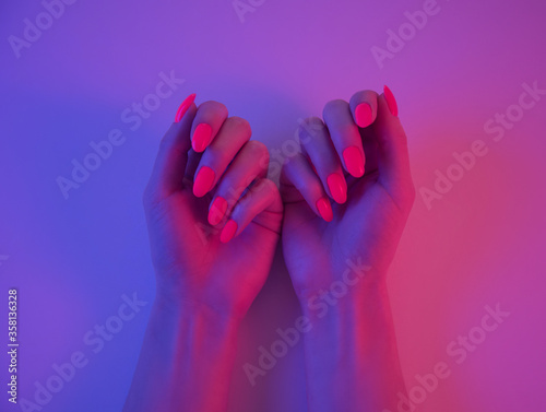 Woman hands with beautiful bright orange manicure in neon light.