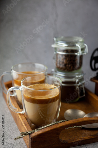 Iced Dalgona coffee drink on wooden tray background. Instant coffee or espresso powder whipped with sugar and hot water. Coffee with milk latte, cappuccino. Two glass cups with double walls. Breakfast