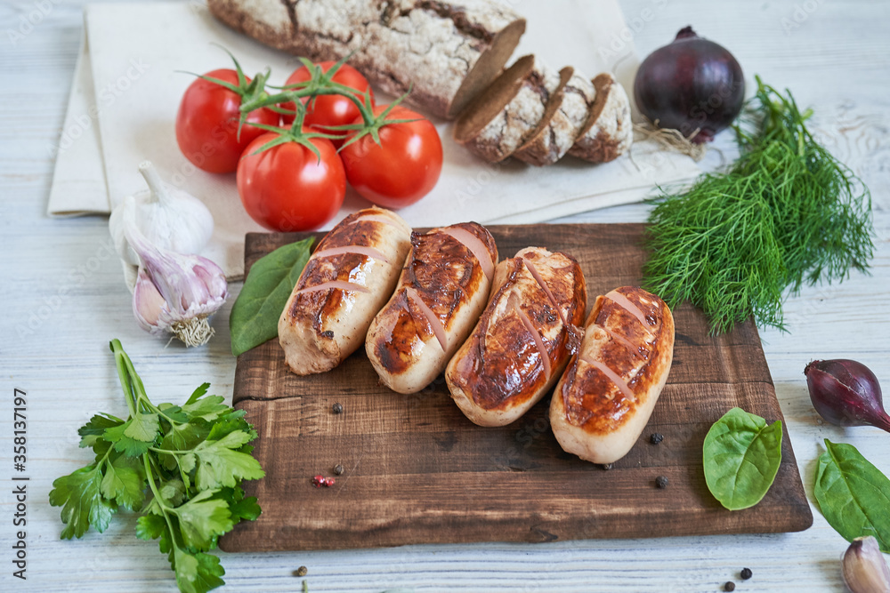 grilled sausages with tomatoes and herbs on the board on white table
