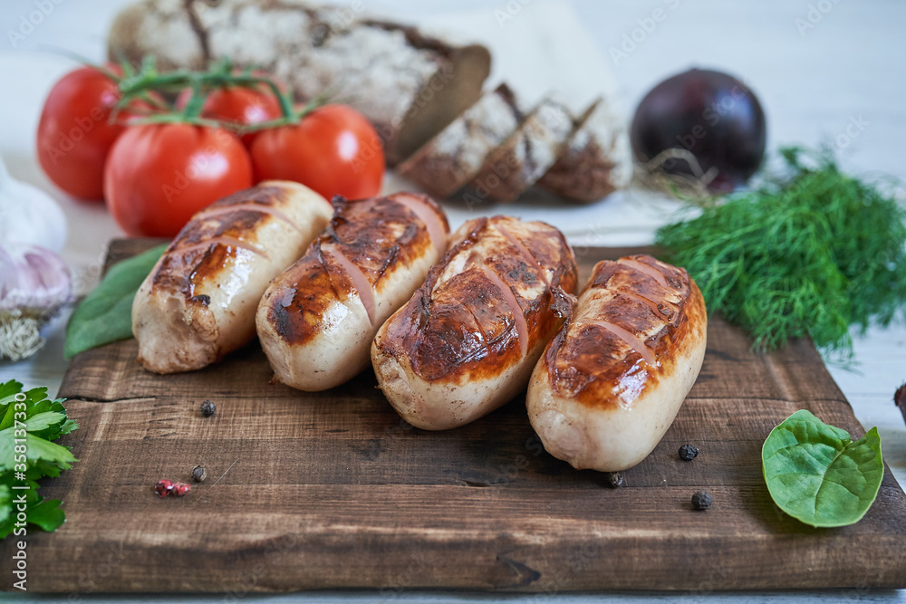 grilled sausages with tomatoes and herbs on the board on white table
