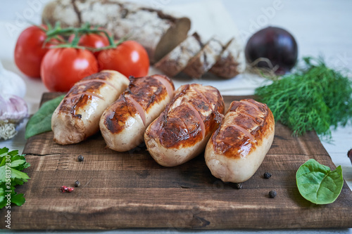Obraz na płótnie grilled sausages with tomatoes and herbs on the board on white table w salonie