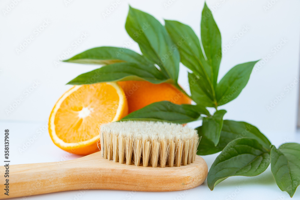 Wooden brush for dry massage with natural bristles on a background of oranges and green leaves. The concept of spa and home body care. Wooden brush for dry massage with natural bristles on a background of oranges and green leaves. The concept of spa and home body care.