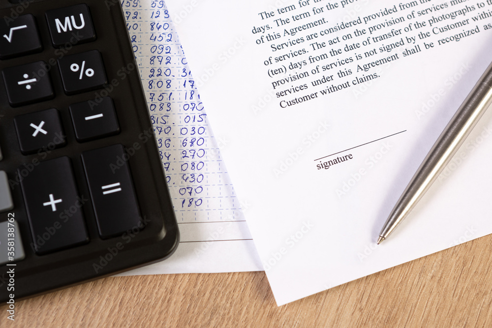 A part of contract or agreement document, space of signature with a silver pen and calculator. A part of contract or agreement document, space of signature with a silver pen and calculator.