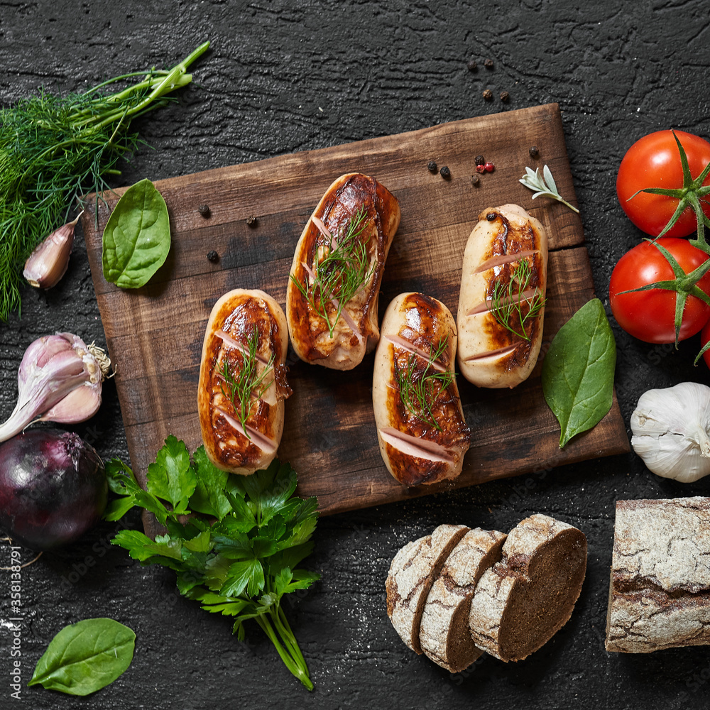 grilled sausages with tomatoes and herbs on the board on a wooden table