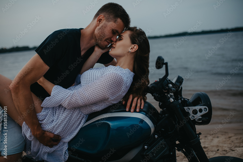 Couple makes love on beach lying on motorcycle.