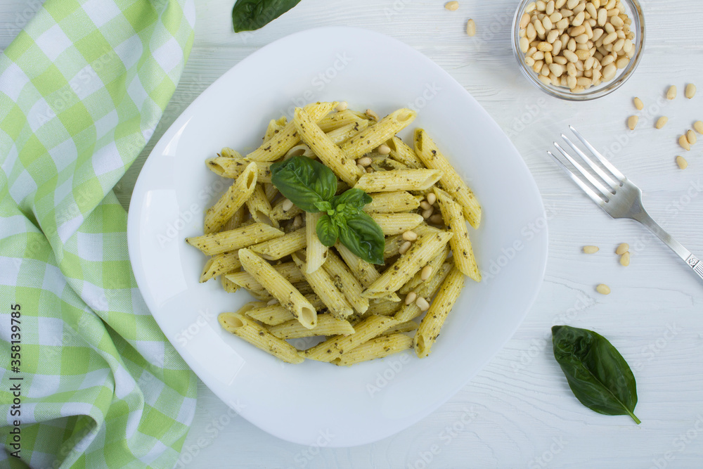 Italian pasta with pesto and pine nuts in the plate on the white wooden background. Top view. Closeup.