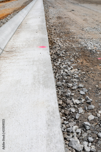 Long view down freshly extruded concrete curb beside road bed under construction, vertical aspect