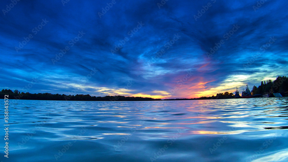 Fantastic dramatic sunset over the river. Overcast clouds in the sky. Picturesque dramatic scene