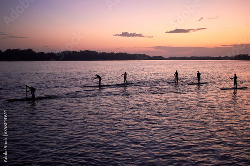 Stand up paddle boarders (SUP) silhouettes on the calm water of the Danube river at dusk in the springtime