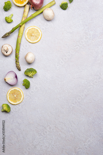 Group of organic fresh vegetables - green asparagus, broccoli, mushrooms on grey background, flat lay. Concept of  healthy vegetarian food, diet and home cooking. Top view, copy space.
