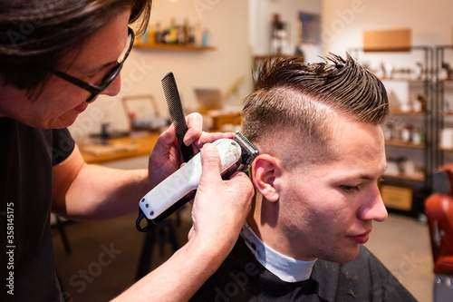 Barber trims the hair of young man with a razor