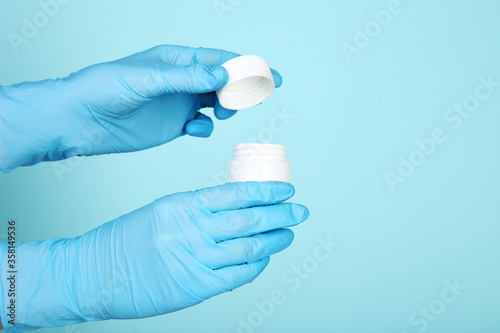 Doctor hands in gloves holding medicine bottle on blue background