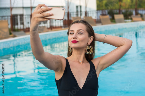 Young beautiful woman doing selfie on a smartphone in the pool. Young sexy woman in the black swimsuit