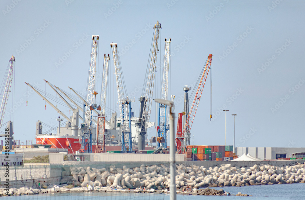 Containers, cranes and cargo ships at the port of Bari, Italy, on a clean day.

