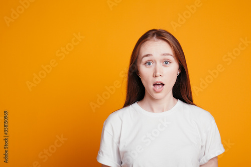 Red haired girl in surprise looks in camera with her mouth open. Portrait photo of the girl is embarrassed and surprised.