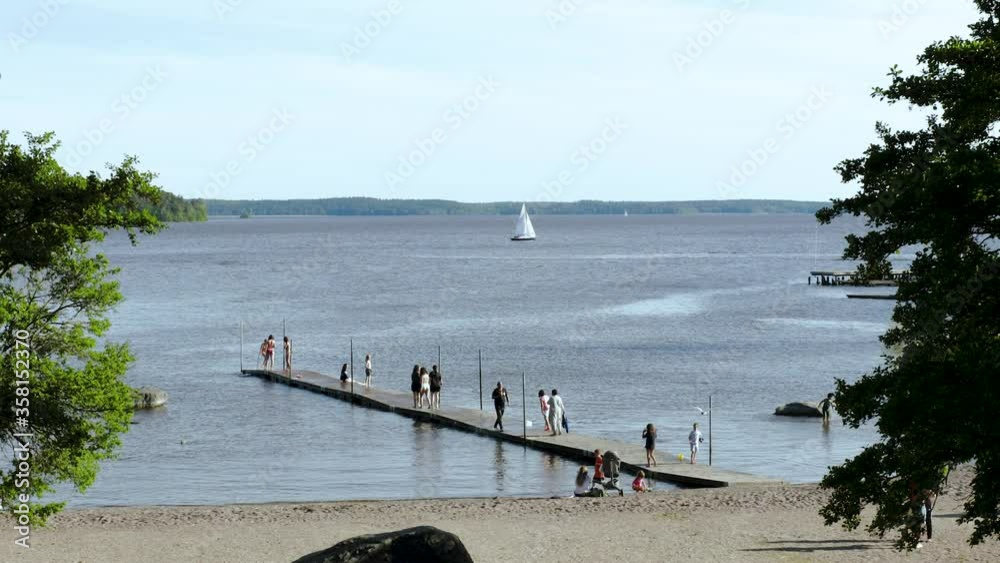 Gorgeous view of lake landscape. People on platform trying water. White sailboat on horizon. Sweden. Europe. Uppsala. Gorgeous view of lake landscape. People on platform trying water. White sailboat on horizon. Sweden. Europe. Uppsala.