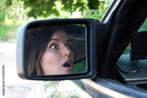 scared face of a girl in a side mirror of a car. Girl driver scared driving a car © natalylad