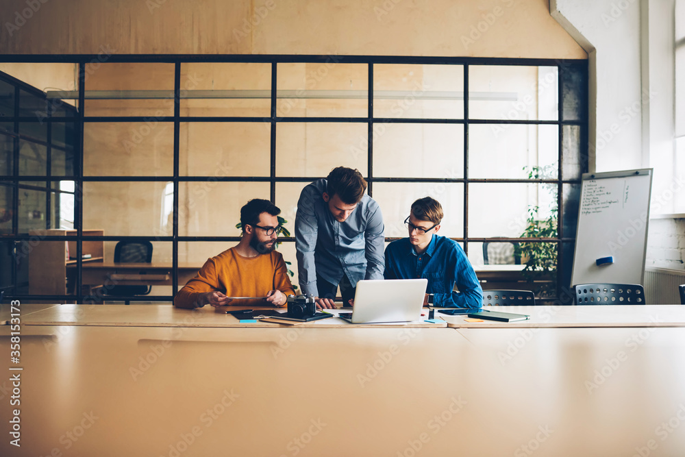 Skilled crew of male coworkers having meeting table for making creative solutions together, group of designers brainstorming during working process using technology for making strategy for startup
