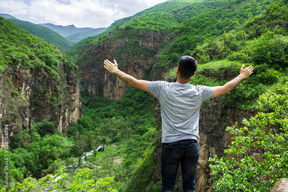 A man with open hands stands by a cliff