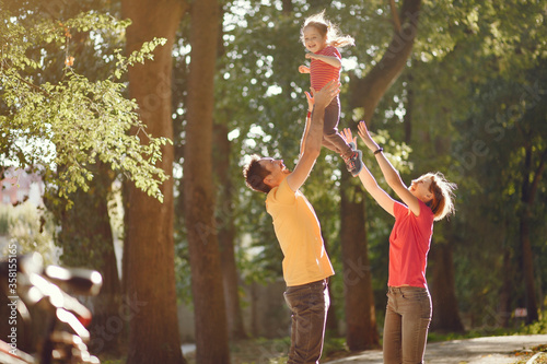 Family with cute little daughter. Father in a yellow t-shirt. People walks in a park.